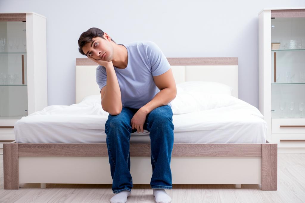 A worried man sitting on the edge of the bed, thinking about his relationship.